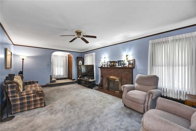 carpeted living room with ceiling fan, ornamental molding, and a brick fireplace