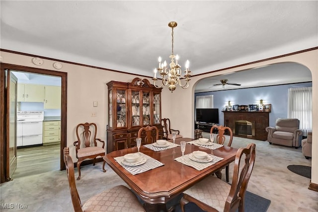 dining area featuring ceiling fan with notable chandelier, light colored carpet, a fireplace, and crown molding