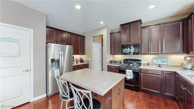 kitchen with black appliances, dark hardwood / wood-style floors, a kitchen island, and a kitchen bar