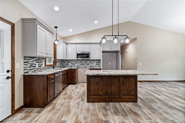 kitchen featuring a center island, light stone counters, light hardwood / wood-style floors, vaulted ceiling, and appliances with stainless steel finishes