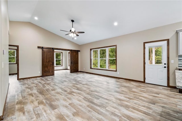 unfurnished living room featuring a barn door, vaulted ceiling, ceiling fan, and a healthy amount of sunlight