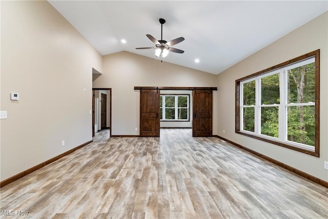 unfurnished living room with ceiling fan, a barn door, light hardwood / wood-style flooring, and vaulted ceiling