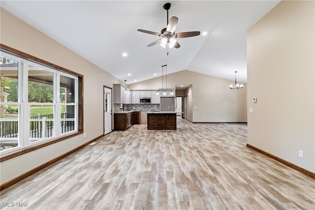 kitchen featuring backsplash, ceiling fan with notable chandelier, vaulted ceiling, a kitchen island, and dark brown cabinetry