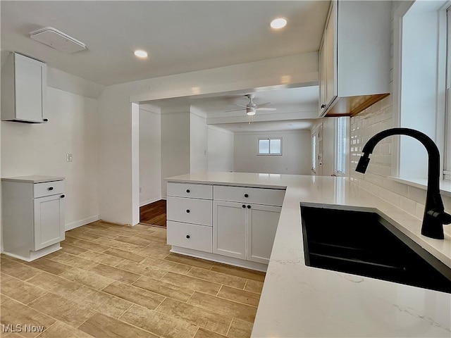 kitchen featuring backsplash, ceiling fan, white cabinetry, and sink