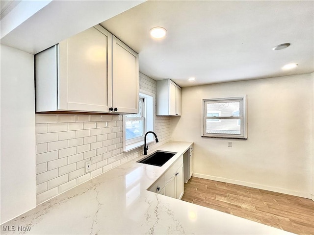 kitchen with sink, light wood-type flooring, tasteful backsplash, light stone counters, and white cabinetry