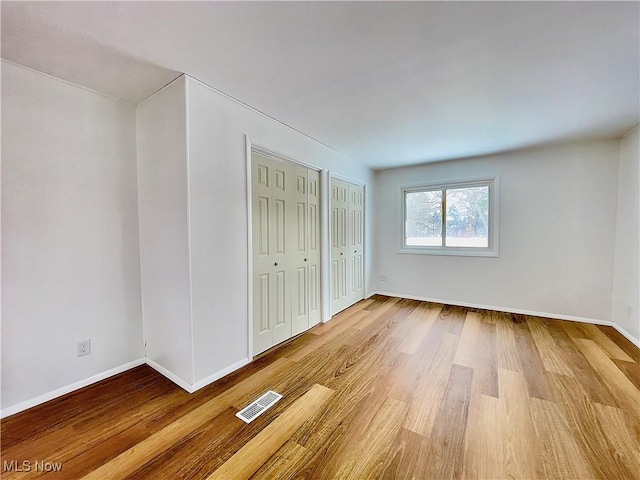 unfurnished bedroom featuring multiple closets and light hardwood / wood-style flooring