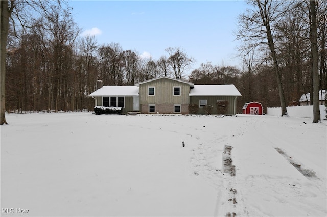 snow covered back of property featuring a storage unit