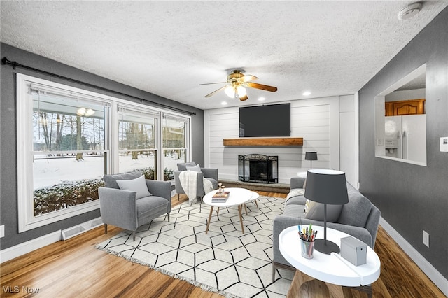 living room featuring ceiling fan, a fireplace, a textured ceiling, and light hardwood / wood-style flooring