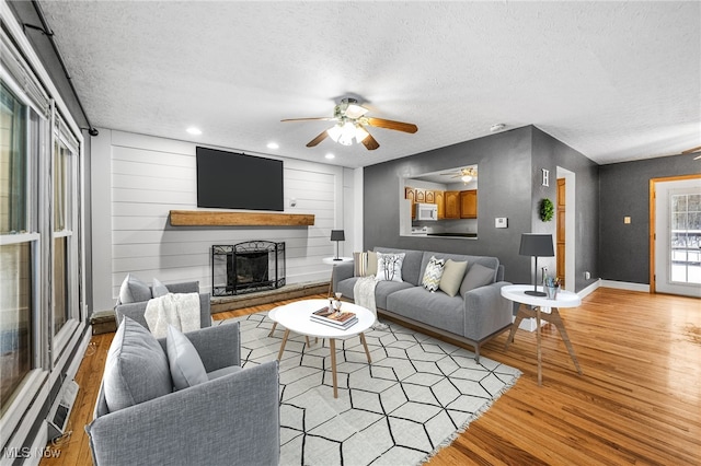 living room featuring ceiling fan, light hardwood / wood-style floors, and a textured ceiling