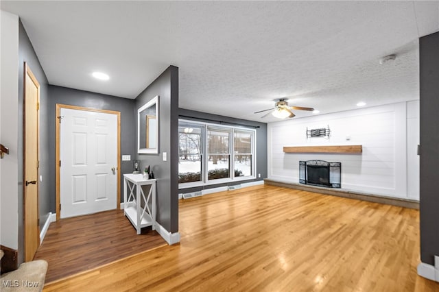 unfurnished living room featuring wood-type flooring, a textured ceiling, a large fireplace, and ceiling fan