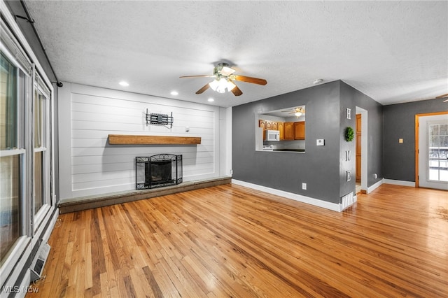 unfurnished living room with ceiling fan, a textured ceiling, and light hardwood / wood-style flooring