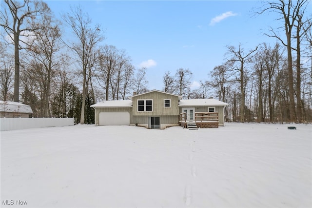 snow covered rear of property with a garage and a wooden deck