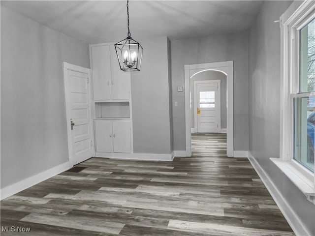 unfurnished dining area featuring dark wood-type flooring and a notable chandelier