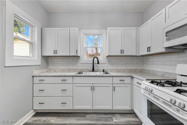 kitchen with white appliances, wood finished floors, a sink, white cabinets, and backsplash