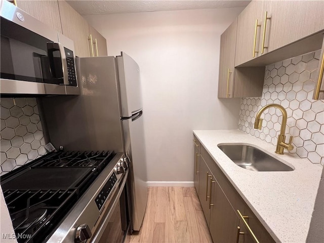 kitchen featuring backsplash, sink, light stone countertops, appliances with stainless steel finishes, and light hardwood / wood-style floors