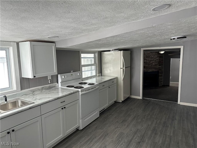 kitchen with a brick fireplace, white appliances, sink, white cabinets, and dark hardwood / wood-style floors