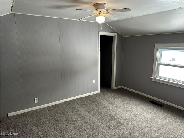 spare room featuring carpet flooring, ceiling fan, wood walls, and vaulted ceiling