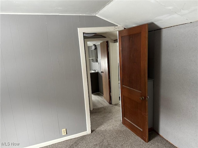 hall featuring carpet floors, wooden walls, and vaulted ceiling