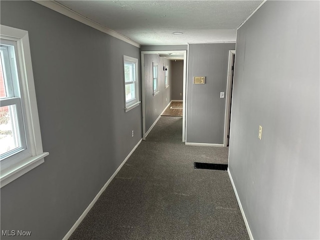 hallway with crown molding, plenty of natural light, a textured ceiling, and dark colored carpet