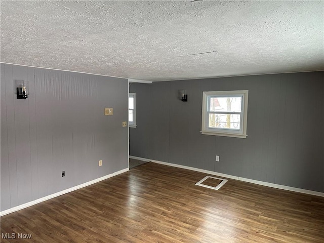 spare room featuring a textured ceiling, dark hardwood / wood-style floors, and a wealth of natural light