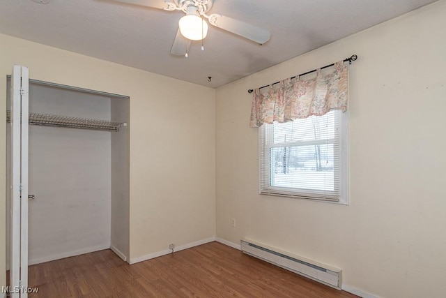 unfurnished bedroom with ceiling fan, a closet, a baseboard radiator, and wood-type flooring