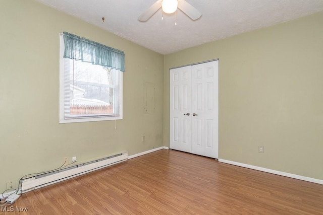 unfurnished bedroom featuring hardwood / wood-style floors, a closet, ceiling fan, and a baseboard heating unit