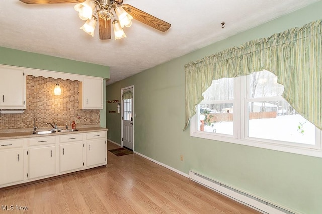 kitchen with decorative backsplash, baseboard heating, sink, light hardwood / wood-style flooring, and white cabinets