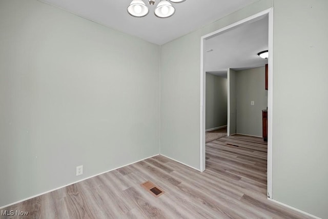 empty room featuring a notable chandelier and light hardwood / wood-style floors