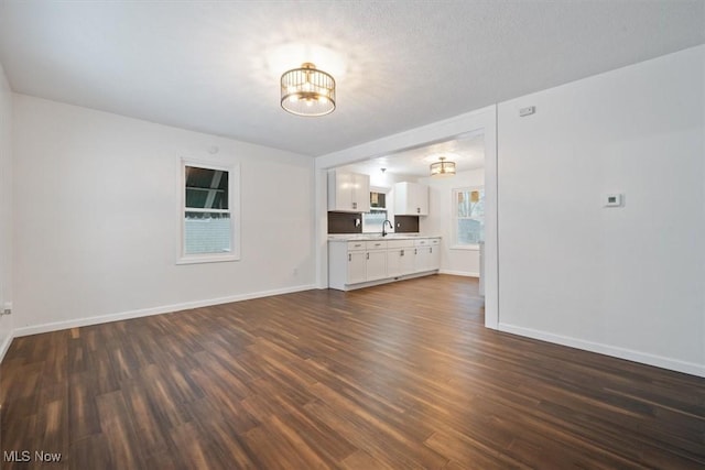 unfurnished living room featuring a textured ceiling, dark wood-type flooring, sink, and a chandelier