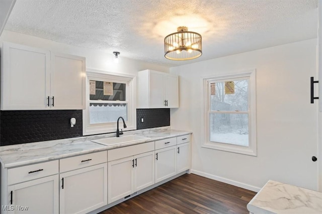 kitchen featuring light stone countertops, dark hardwood / wood-style flooring, sink, a notable chandelier, and white cabinets