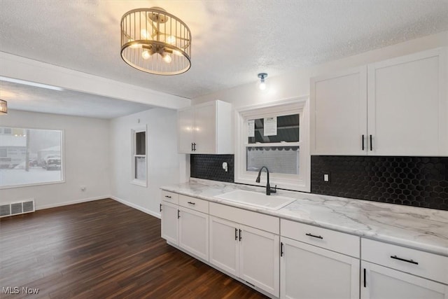 kitchen with decorative backsplash, a textured ceiling, sink, a notable chandelier, and white cabinets