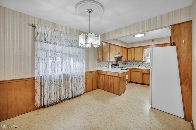 kitchen featuring stove, wooden walls, white refrigerator, decorative light fixtures, and a chandelier