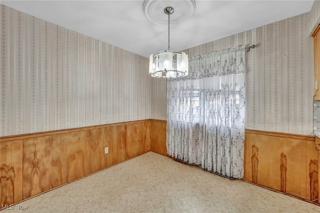 unfurnished dining area featuring wooden walls, carpet floors, and a notable chandelier