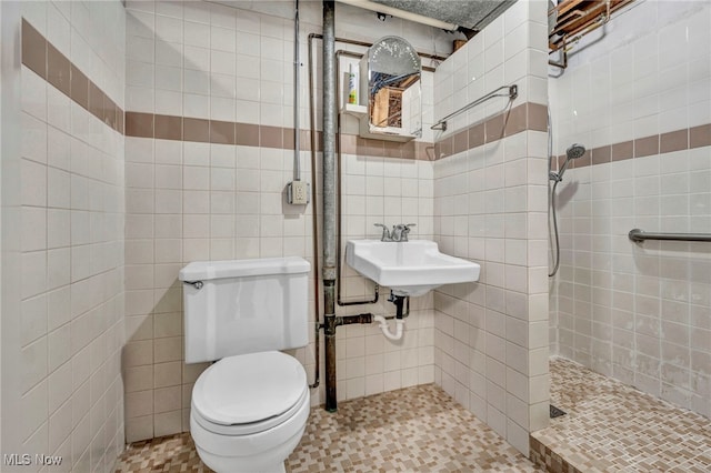 bathroom with a tile shower, sink, tile walls, and toilet