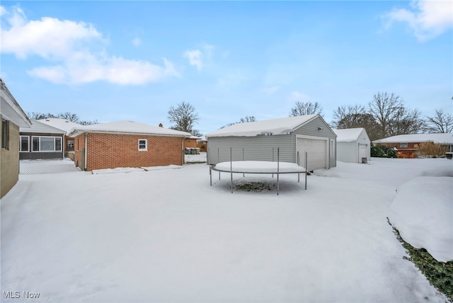 snow covered property featuring an outbuilding, a trampoline, and a garage