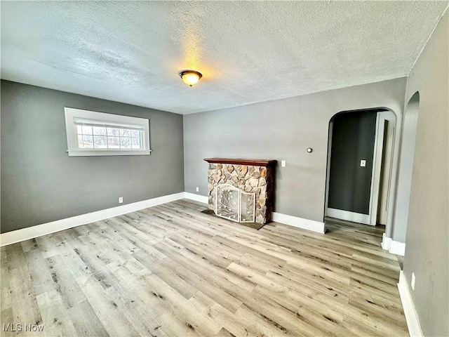 spare room featuring a fireplace, light hardwood / wood-style floors, and a textured ceiling