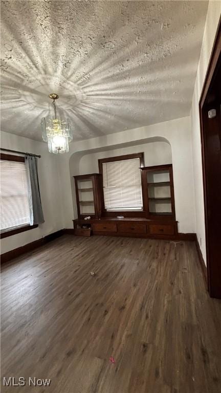 empty room with a textured ceiling, an inviting chandelier, and dark wood-type flooring