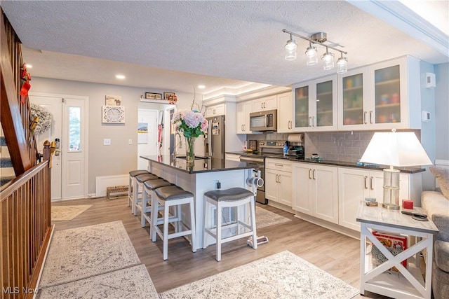 kitchen with a center island, backsplash, light wood-type flooring, white cabinetry, and stainless steel appliances