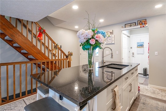 kitchen featuring white cabinetry, a kitchen breakfast bar, hardwood / wood-style floors, dark stone counters, and a kitchen island