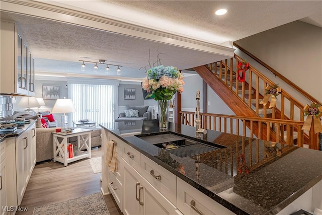 kitchen featuring a textured ceiling, sink, light hardwood / wood-style flooring, dark stone countertops, and white cabinetry