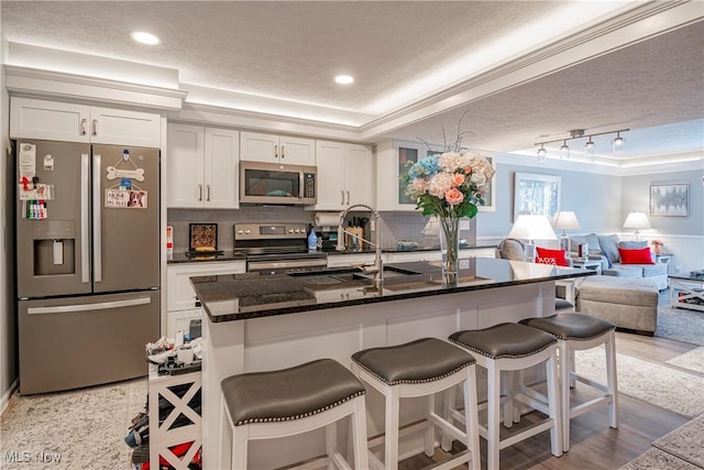 kitchen with a textured ceiling, an island with sink, a kitchen bar, white cabinetry, and stainless steel appliances