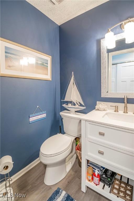 bathroom with hardwood / wood-style flooring, vanity, toilet, and a textured ceiling