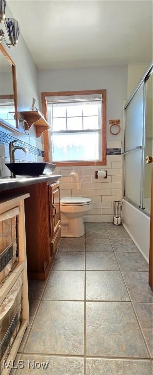 full bathroom featuring vanity, tile walls, enclosed tub / shower combo, tile patterned flooring, and toilet