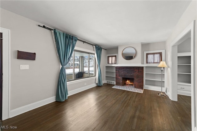 unfurnished living room featuring built in features, dark hardwood / wood-style floors, and a brick fireplace