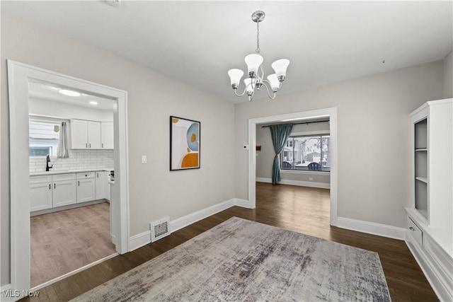 dining area featuring an inviting chandelier, a wealth of natural light, dark wood-type flooring, and sink