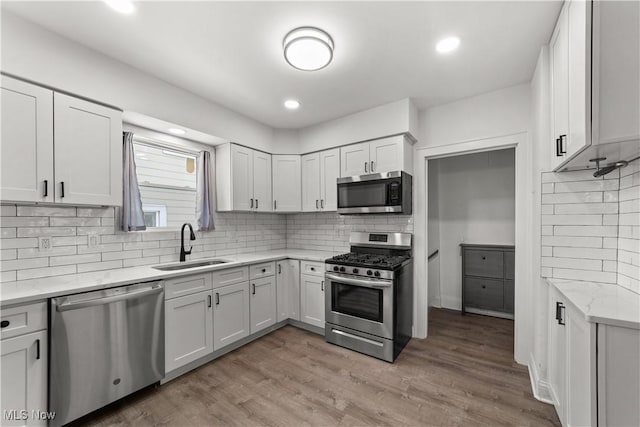 kitchen featuring sink, tasteful backsplash, light hardwood / wood-style floors, white cabinets, and appliances with stainless steel finishes