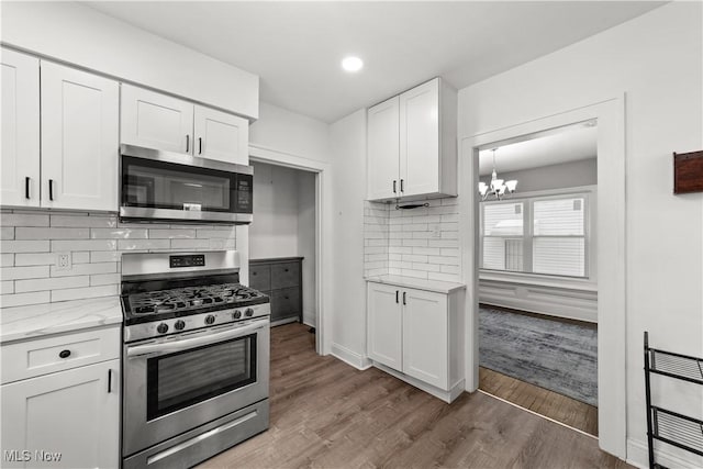 kitchen with appliances with stainless steel finishes, backsplash, light stone counters, wood-type flooring, and white cabinets