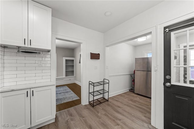 kitchen with stainless steel fridge, backsplash, light hardwood / wood-style flooring, and white cabinetry