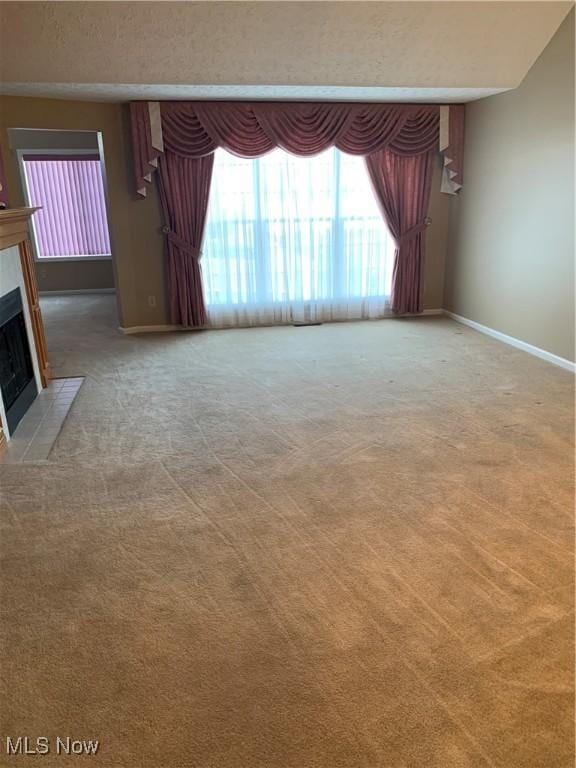 carpeted empty room with lofted ceiling and a tiled fireplace