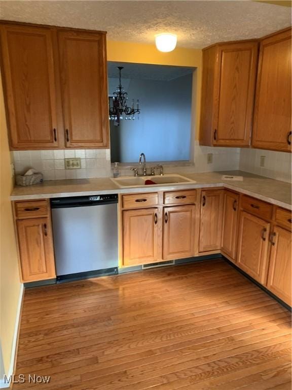 kitchen with sink, an inviting chandelier, light hardwood / wood-style flooring, stainless steel dishwasher, and decorative light fixtures